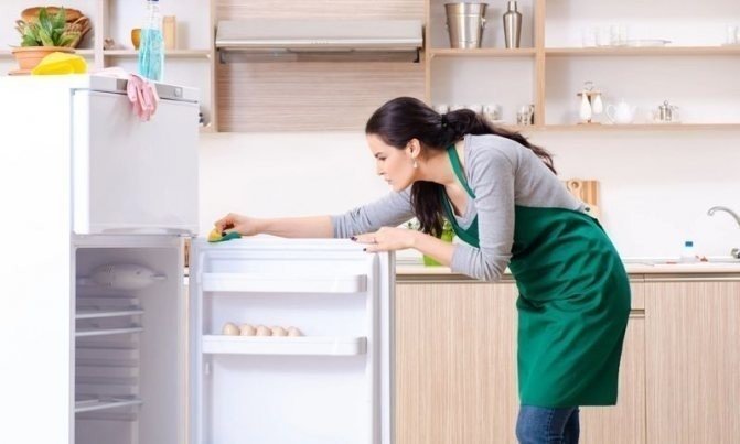 Женщина моет холодильник