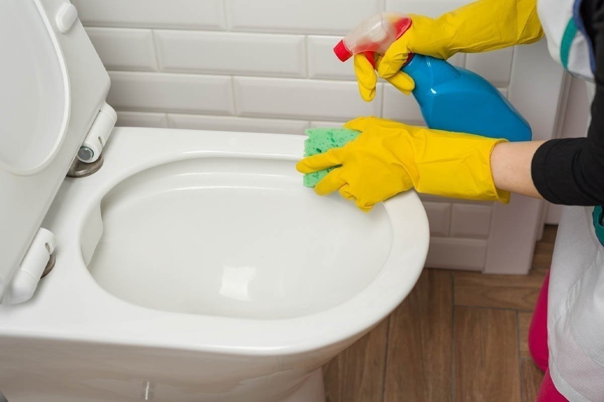 Уборщица в резиновых перчатках моет туалет